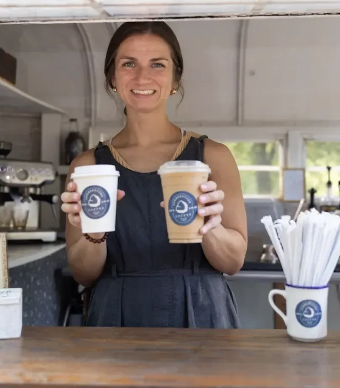 A Cornerstone Coffee barista holding two branded cups at the event coffee bar