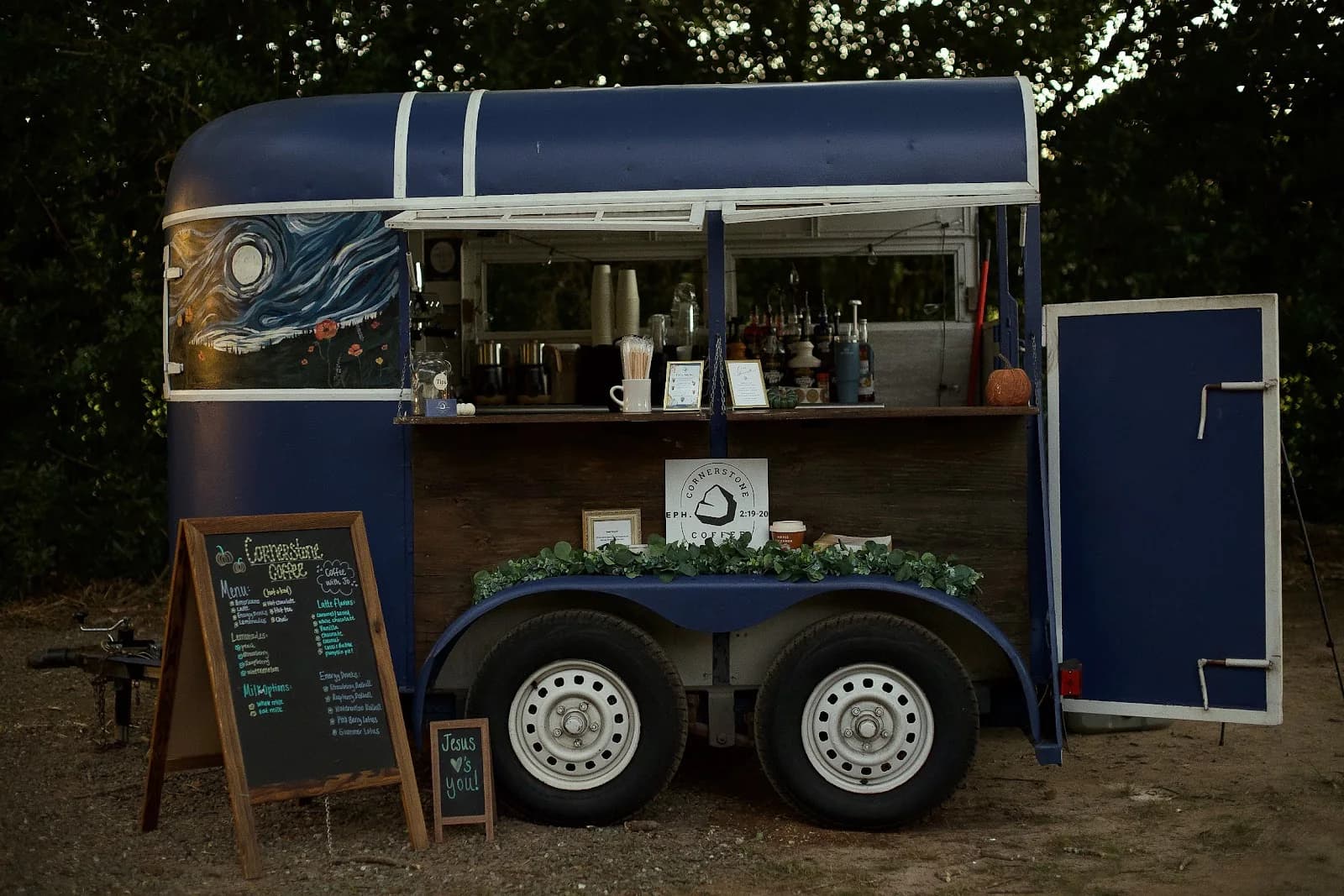 The Cornerstone Coffee trailer open and lit for an evening event, chalkboard menu out front