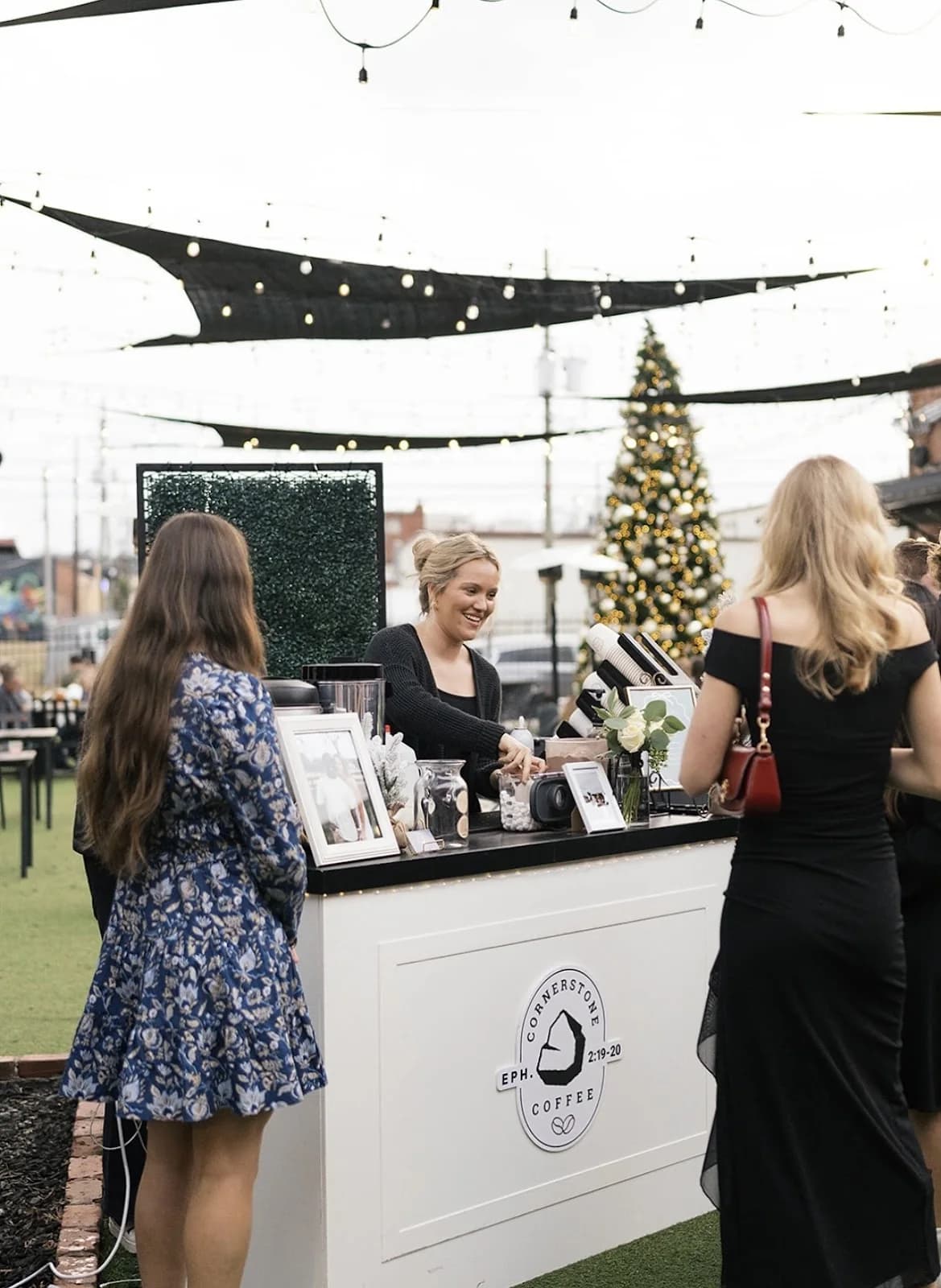 Guests ordering drinks at the Cornerstone Coffee cart during a holiday event under string lights