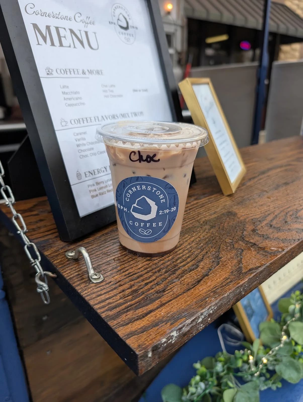 A branded Cornerstone Coffee iced latte on a wooden table beside the event menu